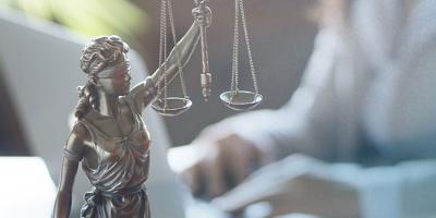 Lady Justice statue with scales, with a blurred person working in the background.